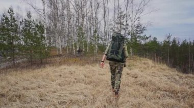 Sırt çantalı genç adam gündüz vakti ormanda yürüyor, ağır çekimde. 