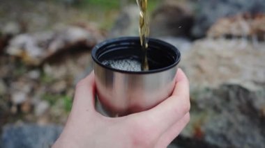 Kadın termos şişesinden metal bardağa çay dolduruyor. Yavaş çekim görüntüleri.
