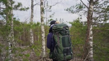 Sırt çantalı genç bir kadın gündüz vakti ormanda yürüyor, ağır çekim. 