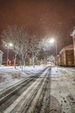 Ağaçlar ve binalarla çevrili karlı yolun üzerindeki gece aydınlanmasının manzarası 