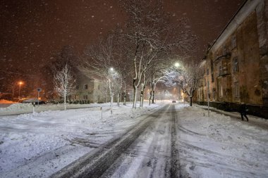 Ağaçlar ve binalarla çevrili karlı yolun üzerindeki gece aydınlanmasının manzarası 