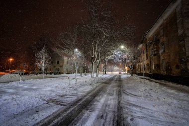 Ağaçlar ve binalarla çevrili karlı yolun üzerindeki gece aydınlanmasının manzarası 