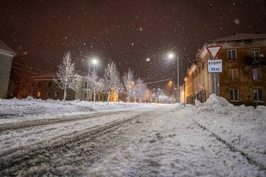 Ağaçlar ve binalarla çevrili karlı yolun üzerindeki gece aydınlanmasının manzarası 