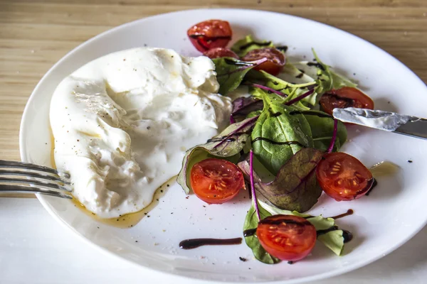 Burrata mozzarella kiraz domates ve yeşil marul ahşap arka plan üzerinde beyaz plaka