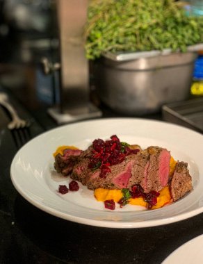 Biftek, kabak püresi ve fırında pancar, beyaz bir tabakta, bir restoranda.