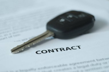 Masanın üzerinde bir sözleşme ve araba anahtarları var, vurgu belgenin adı ve anahtarlar üzerinde. Bulanık resim.