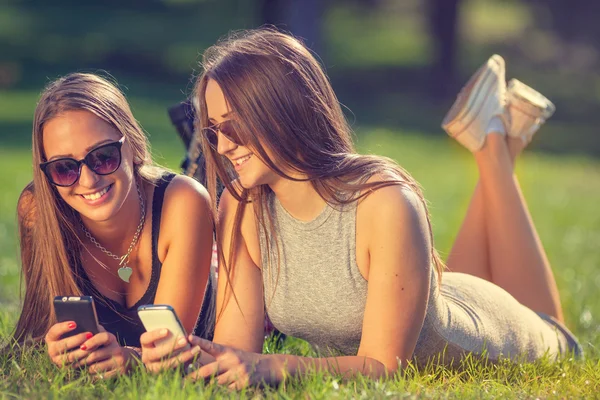 Dos chicas jóvenes sonriendo y usando sus teléfonos inteligentes —  Fotos de Stock