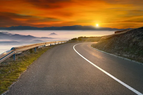 Driving on asphalt mountain road towards the sun — Stock Photo, Image