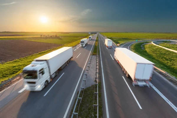 Grote witte vrachtwagens op de snelweg naar de ondergaande zon — Stockfoto