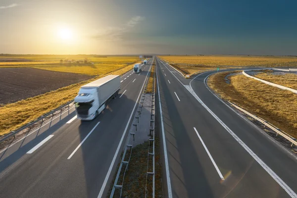 Grote witte vrachtwagens op de lege snelweg bij zonsondergang — Stockfoto