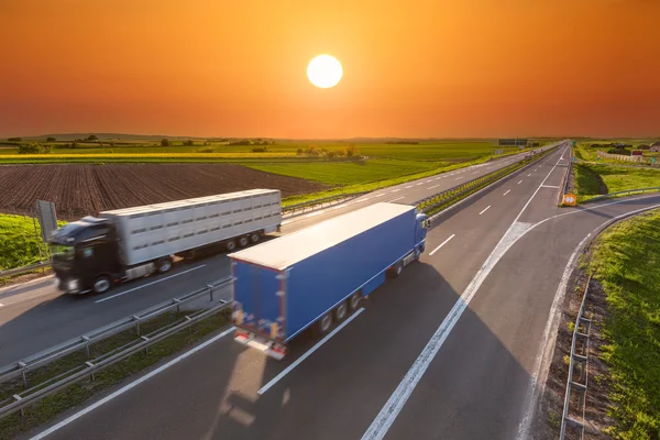 Snelle levering vrachtwagens op de lege snelweg bij zonsondergang — Stockfoto