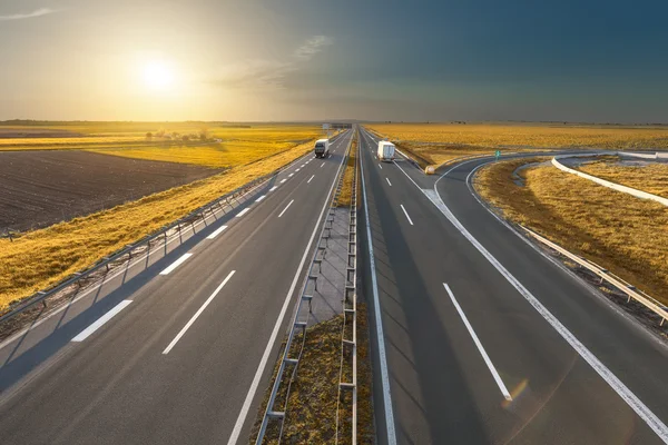 Дві самотні вантажівки на порожньому шосе на заході сонця — стокове фото