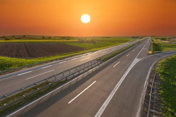 Offene Autobahn durch beleuchtete grüne Felder — Stockfoto