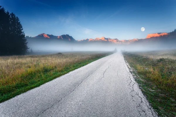 Empty road towards the mountain peaks at dawn — Stock Photo, Image