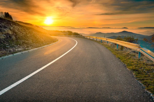 Driving on mountain road against the rising sun — Stock Photo, Image