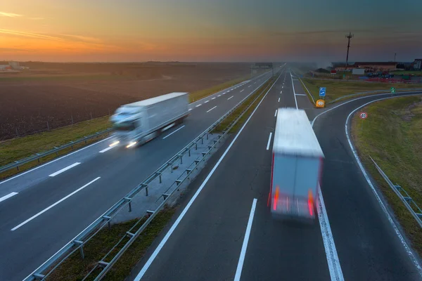 Kierowcy ciężarówek w ruchu rozmycie na autostradzie na zachodzie słońca — Zdjęcie stockowe