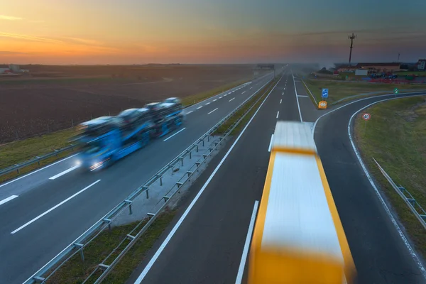 Två lastbilar i rörelse oskärpa på motorvägen vid solnedgången — Stockfoto