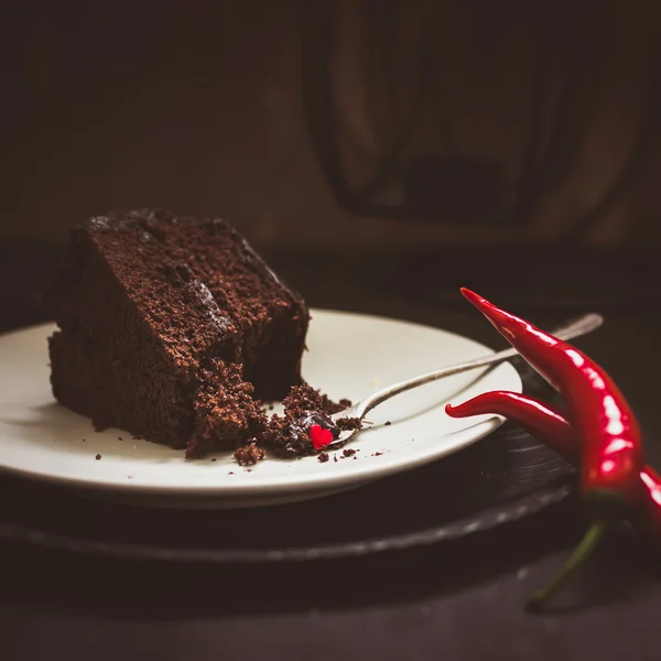 Piece of dark chocolate cake and red hot peppers — Stock Photo, Image