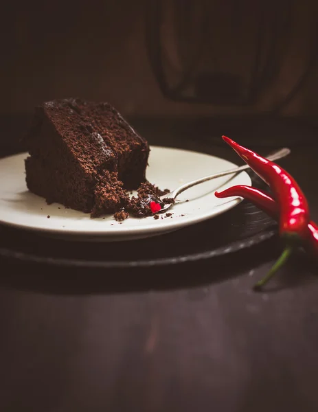 Piece of dark chocolate cake and red hot peppers — Stock Photo, Image