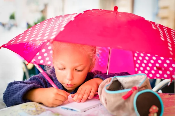 Linda menina loira sentada na mesa sob seu guarda-chuva rosa — Fotografia de Stock