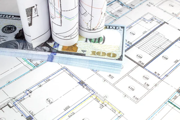 Construction drawings and money against the background of the plan of the building under construction.
