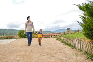 Koruyucu maskeli bir anne ve oğul el ele yürüyorlar, covid-19.