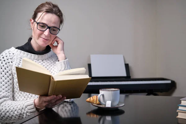 Gülümseyen kadın evde kitap okuyor.