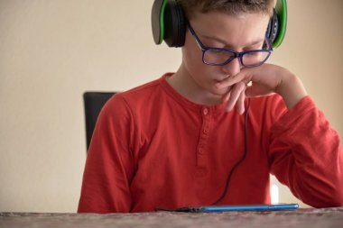 Çocuk evde oturmuş kulaklıkla cep telefonunu kullanıyor.