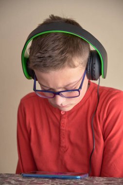 Çocuk evde oturmuş kulaklıkla cep telefonunu kullanıyor.