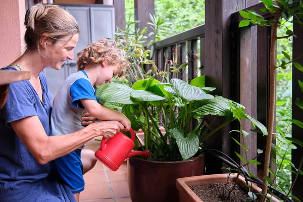 Anne oğluyla birlikte balkonda çiçekleri suluyor.