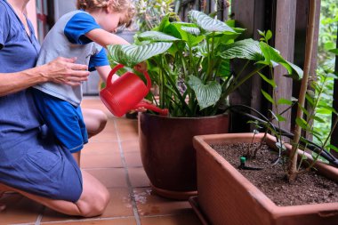 Çocuk çiçekleri sularken annesi onu izliyor.