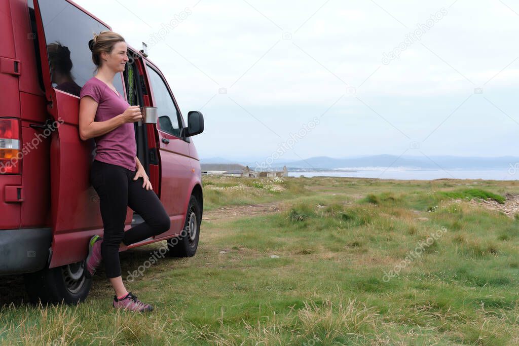 Woman holding a cup in her hand next to her motorhome on her summer holiday.