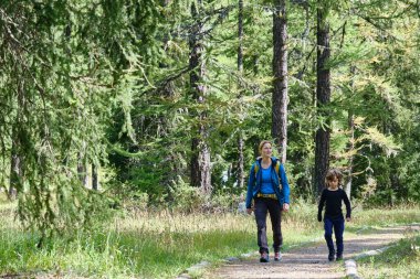 Sırt çantalı bir kadın oğluyla ormanda yürüyor.