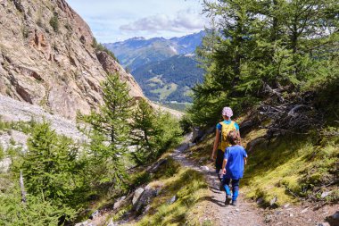 Bir anne ve oğlunun, dağlarda yürüyüş yaparak doğanın tadını çıkarışının arka görüntüsü.