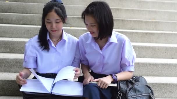Okul üniforması Sevimli Asya Tay liseli kız öğrenci çift mutlu gülümseyen yüzü ile üçüncü bir kişi öğretmen veya eğitmen ile ev ödevi veya sınav tartışırken merdiven üzerinde oturmak. — Stok video