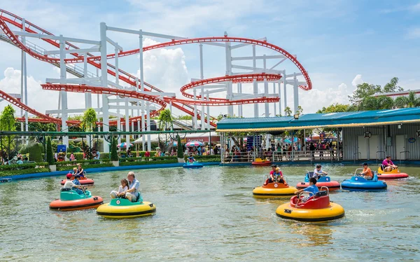 Mensen met verschillende leeftijd speelt reddingsboei-vorm boot met achtergrond van de achtbaan in het pretpark — Stockfoto