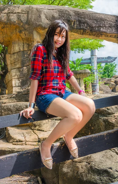 Cute Thai girl is sitting on the wooden fence — Stock Photo, Image