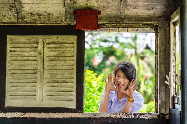 Süße asiatische Schülerin in Uniform überrascht durch die alte Retro-Fensterscheibe. Wird irgendjemand Angst bekommen? — Stockfoto