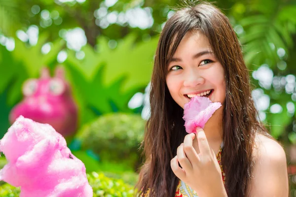 Mignonne asiatique thaï fille est manger rose candyfloss avec joie dans lumineux été dans la nature vert fond concept version — Photo