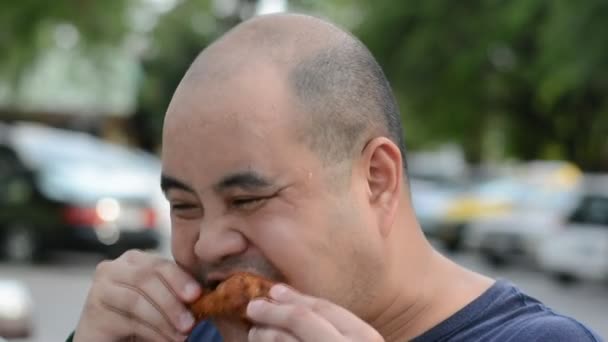 Gordo asiático calvo cabeza tailandesa hombre está mordiendo y comiendo pollo frito muslo avariciosamente con hambre con sudor de agua en su cara en 1920x1080 calidad HD. Podría asfixiarse debido a su glotonería. Vídeo Stock — Vídeo de stock