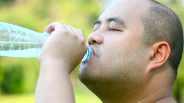 太ったアジアのはげ頭男の顔の表情は、暑い夏の熱中症を防ぐためにペットボトルの渇きで水を飲んでいます. — ストック動画