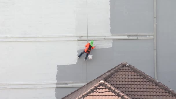 Trabalhador do trabalho asiático está trabalhando por enforcar-se, pintando a parede lateral do edifício em canteiro de obras industriais. Precisa de mais precauções de segurança. . — Vídeo de Stock