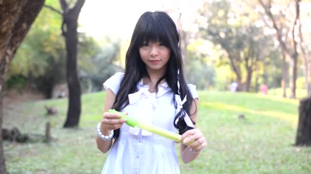 ヴィンテージのファッション服ドレスでかなりアジアのタイの女の子がかわいい幸せな表情で彼女の子供のおもちゃを思い出させるために公園でシャボン玉を吹いています。 — ストック動画