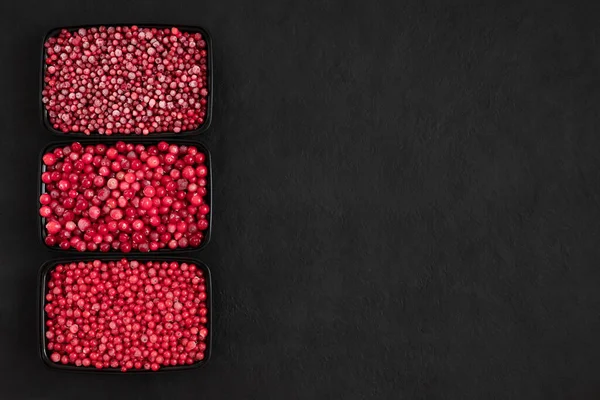 Frozen berries mix in plastic containers on a black background. Cranberries, red currants, cowberries. Space for text. Top view, flat lay.
