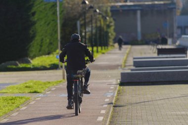 Yaşlı adam kaldırımdan aşağı bisiklet sürüyor. Kaldırımlar tuğla bir yolun yanında. Kaldırımda birkaç bank var.
