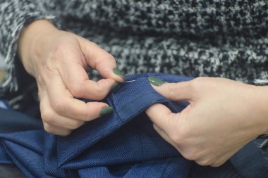 Bir kadın mavi bir kumaş parçasını iğneyle dikiyor.