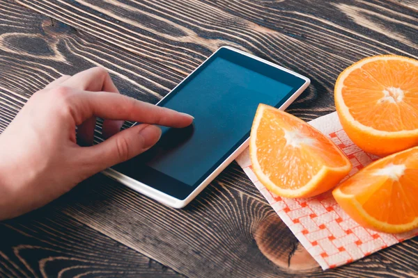 Mujer usando teléfono móvil contra naranjas de frutas. Concepto de tecnología . — Foto de Stock