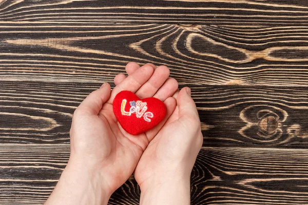 Mens mãos segurando coração vermelho sobre fundo de madeira — Fotografia de Stock