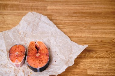 Parşömen kağıdında baharatlı iki çiğ balık bifteği. Dokulu ahşap mutfak masası. Seçici odak.