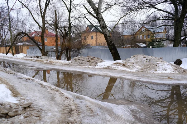 Dirty snow and puddles on the road. Gloomy spring countryside landscape.